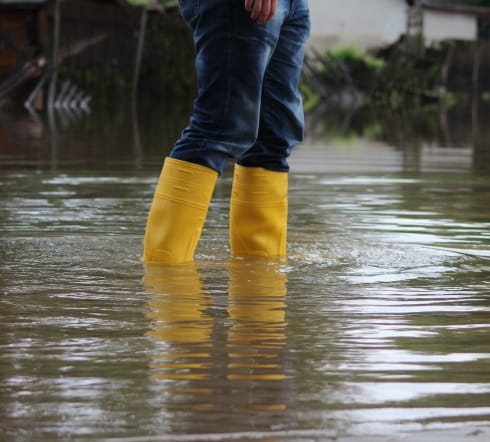 image of a person walking through a flooded area, glad at the fact they have flood insurance with the best inaurnace agency in Foley, AL