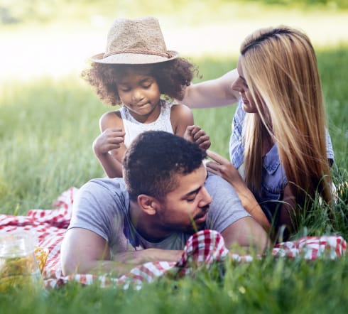 image of a family; mother and father laying on the grass with their baby overjoyed with their new Univeral Life Insurance Policy from the best insurance agency in Foley, AL